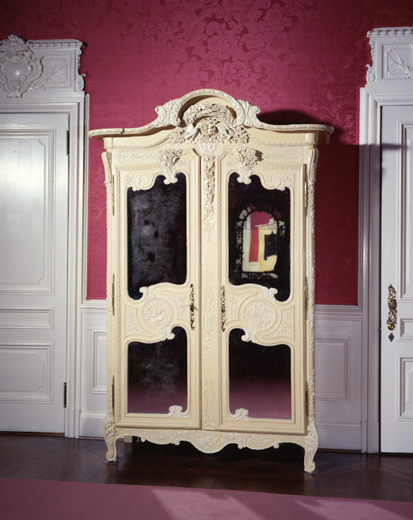French Armoire: This oak armoire, made in the upper Normandy town of Fécamp in the early 19th century, would have been unpainted originally. Its front is carved with images of birds, plants, musical instruments, and tools. Armoires of this type were usually made as wedding gifts, and their carvings symbolized family, love, abundance, and prosperity. As part of the restoration of Mrs. Mills's bedroom to its 1890s appearance, conservators stripped away an outer layer of white latex paint from the armoire to reveal two different shades of yellow, believed to have been added when the armoire's mirrors were installed in the 1880s. The armoire is one of the few antique pieces of furniture chosen for Mrs. Mills's Allard et Fils-designed bedroom. It may have been added to the room by Stanford White, the architect of the mansion's expansion.